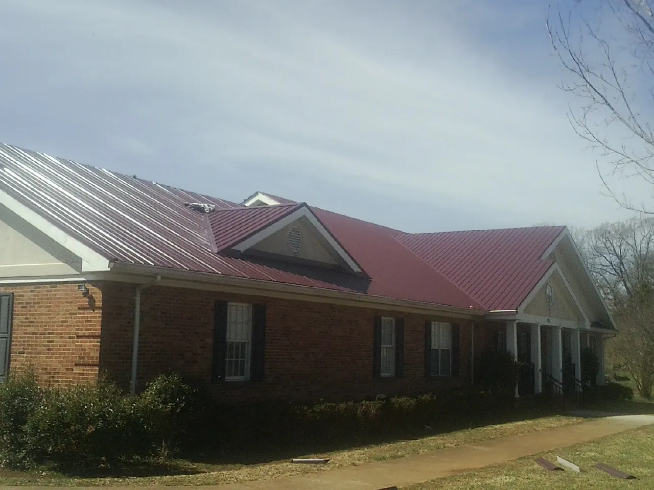 Red metal roof with gabled entries on a long brick building, from a Hail Damage Roof Repair job in Staunton