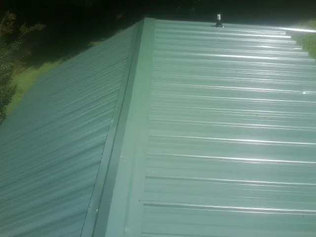 New green metal panels meeting at the ridge of a roof — Flat Roof Repair work by our crew in Staunton