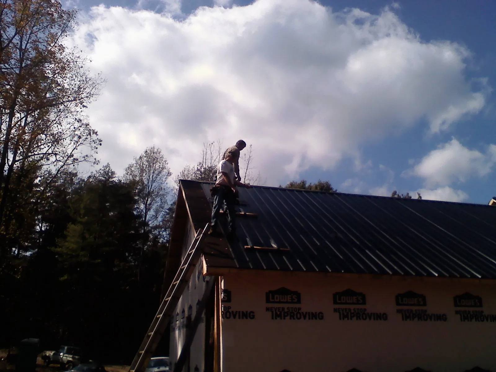 Roofer fastening dark metal panels high against a cloudy sky in Staunton