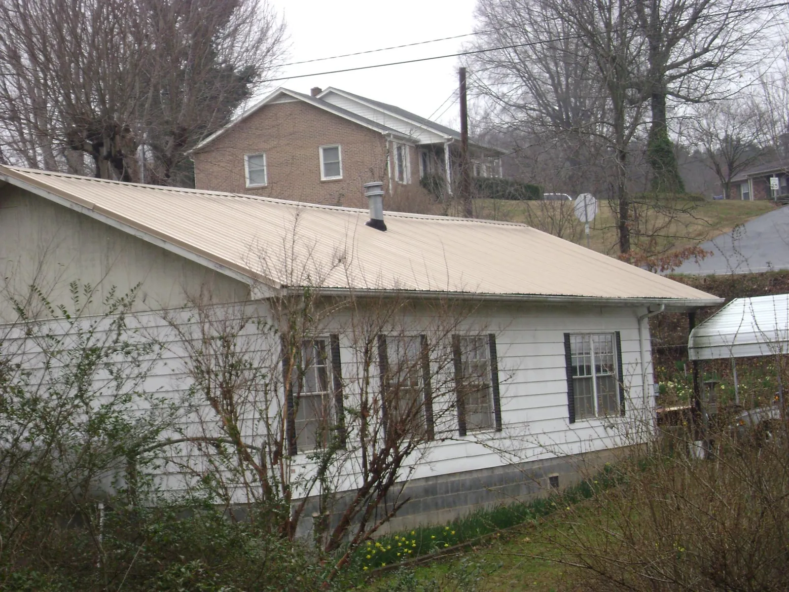 Tan metal roof on a white sided house set into a hillside — Commercial Roofing by Roofing Brothers in Staunton